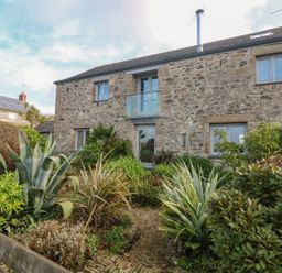 Stone house with multiple windows and a glass balcony above the door surrounded by various green plants at An Skyber in Perranuthnoe