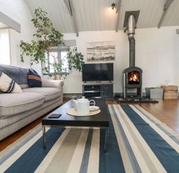 A living room with a sofa coffee table television and a wood burning stove at An Skyber in Perranuthnoe
