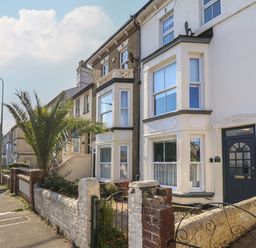 A row of terraced houses with bay windows and small front gardens on a street with a palm tree at First Light in Pakefield near Lowestoft