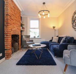 A living room with a brick fireplace a blue rug and grey and blue seating at First Light in Pakefield near Lowestoft