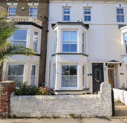 Exterior view of a white terraced house with a black front door and bay windows with a white brick wall and small garden in front at First Light in Pakefield near Lowestoft
