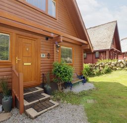 An exterior view of a wooden lodge with a front door at Thistle Dubh ('Doo') Sandyhills