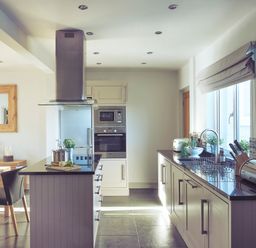 A kitchen with white cabinets black countertops built in oven and microwave and a dining table with black chairs at Craster Reach in Craster