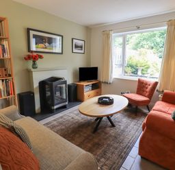 A living room with two sofas, an armchair, a coffee table, a bookshelf, a fireplace, and a window showing a garden at Little Hallgarth in Keswick