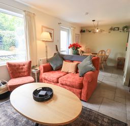 A living room with an orange sofa and chair next to a wooden coffee table and a dining table in the background at Little Hallgarth in Keswick