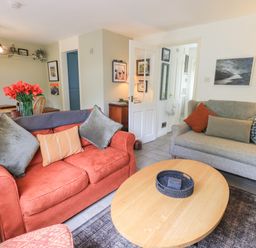 A living room with two sofas a wooden coffee table and a dining table with flowers at Little Hallgarth in Keswick