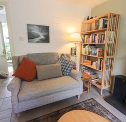 A small living room with a gray sofa with cushions a wooden bookshelf with books and a standing lamp at Little Hallgarth in Keswick