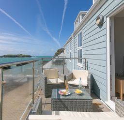 A balcony with wicker furniture and a glass table overlooking the sea at Rebecca in Mullion Cove near Mullion