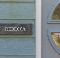A nameplate reading Rebecca mounted on a blue wooden wall next to a gray door with a window at Rebecca in Mullion Cove near Mullion