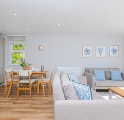 A living room and dining area with grey sofas blue cushions wooden dining table and chairs and framed pictures on the wall at Rebecca in Mullion Cove near Mullion