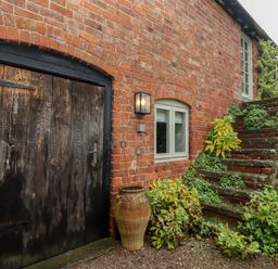 Exterior view of a brick building with a large wooden door small window stone steps and plants at Millpond Bothy in Woolhope
