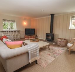 A living room with a sofa, armchairs, a wood-burning stove, a television, and a rug at Millpond Bothy in Woolhope