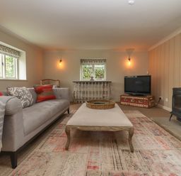 A living room with a sofa ottoman rug television and wood stove at Millpond Bothy in Woolhope