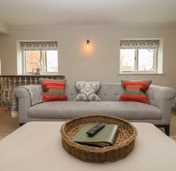 A living room with a gray sofa with patterned cushions and a wicker tray on an ottoman at Millpond Bothy in Woolhope