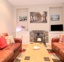 A living room with two leather sofas a wooden coffee table a stone fireplace a TV and framed pictures on the wall at Myrtle Cottage in Windermere