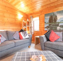 A living room with grey sofas and patterned cushions wooden walls and a large landscape photo at Hayeswater Lodge Burnside Park near Keswick