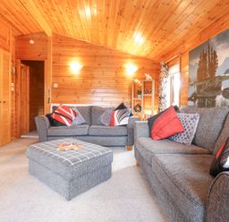 A living room with two grey sofas an ottoman and wood paneled walls at Hayeswater Lodge Burnside Park near Keswick