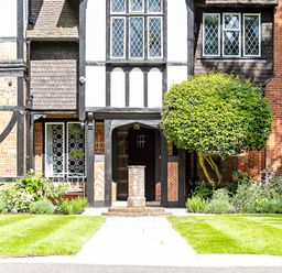 The front entrance of a Tudor style house with a pathway, trimmed lawn and a shaped tree at Tudor Grange in Bournemouth