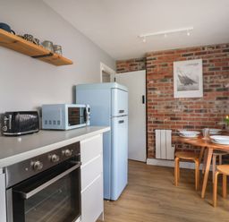 A kitchen with a blue refrigerator microwave black toaster and a dining table with chairs and yellow flowers at 8 Biddlecombe Orchard in Bridport