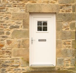 A cream colored door with a mail slot and small window set in a stone wall at Bridge End Cottage in Wark