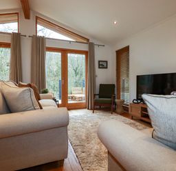 A living room with beige sofas a green armchair a television and wooden-framed windows at 1 Streamside in Lanreath