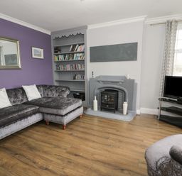 A living room with a grey sectional sofa a bookshelf a fireplace and a TV on a stand at Tan Y Fron in Dyffryn Ardudwy