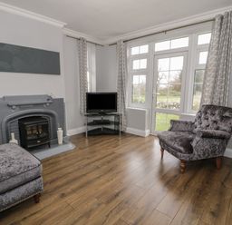A living room with a fireplace television armchair and window with curtains at Tan Y Fron in Dyffryn Ardudwy