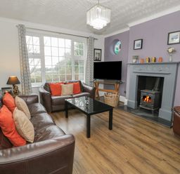 A living room with brown leather sofas orange and beige cushions a black coffee table a fireplace with a wood burning stove and a flat screen TV at Tan Y Fron in Dyffryn Ardudwy