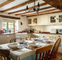 A kitchen with a dining table set with plates glasses and cutlery under exposed wooden ceiling beams at Hope Cottage in Longborough