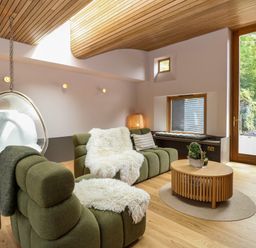 A living room with green sofas a hanging chair a wood coffee table and large windows at Oak Cottage in Somerleyton
