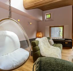 A living room with a hanging egg chair and green sofa with a white throw at Oak Cottage in Somerleyton