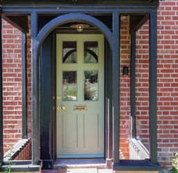 A green front door with four glass panels and a letterbox in a brick wall with black wooden frame
