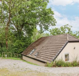 A sloped roof building surrounded by trees and gravel paths at Crystals in Hatherleigh