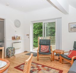 A living room with wooden floor chairs and a sliding glass door leading outside at Crystals Hatherleigh
