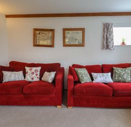 A living room with two red sofas and patterned cushions at Butterton Cottage Combe Raleigh near Honiton