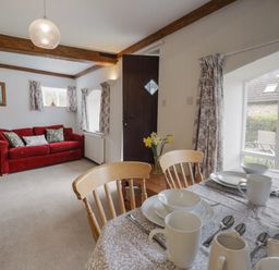 A living room with red sofas wooden dining chairs and a table set with white dishes at Butterton Cottage in Combe Raleigh near Honiton