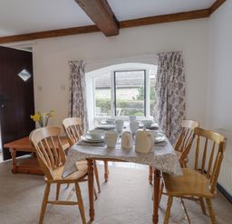 A dining room with a wooden table set for four and wooden chairs near a window at Butterton Cottage in Combe Raleigh near Honiton
