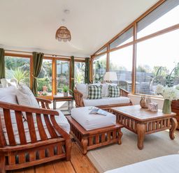 A sunroom with wooden furniture and large windows at Burlodge Swimbridge near Barnstaple