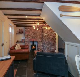 A living room with a stone fireplace two sofas wooden paddles on the wall and a wooden table at The Nook in Brixham