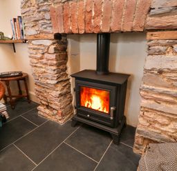 A wood burning stove inside a stone fireplace with a leather chair and a small table nearby at The Nook in Brixham