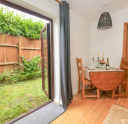 A dining area with a small wooden table set for two and chairs next to open glass doors leading to a garden at Coldharbour Farm Bungalow Annexe Coldharbour near Wareham