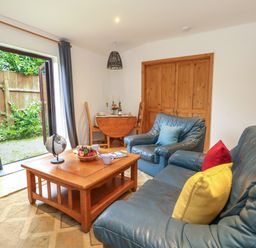 A living room with blue leather sofas a wooden coffee table and open doors to a garden at Coldharbour Farm Bungalow Annexe in Coldharbour near Wareham