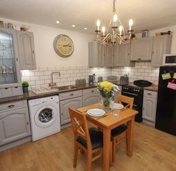 A kitchen with grey cabinets a wooden table set for two a washing machine a black refrigerator and a stove at The Old Sorting Office in Hawarden