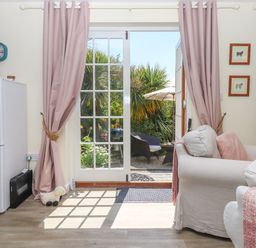 A living area with armchairs and pink curtains by glass doors opening to a garden at Sunset Cottage in Swimbridge near Barnstaple