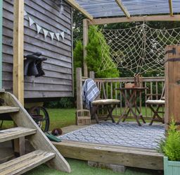 An outdoor wooden deck with two chairs and a table under a pergola with netting at Burr 1 Shepherds Hut in Barnstaple