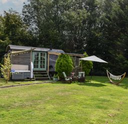 A garden with two wooden chairs and umbrella near a wooden hut on grass at Burr 1 Shepherds Hut in Barnstaple