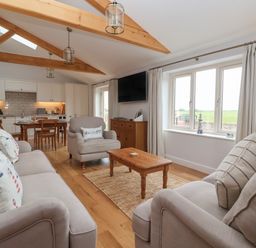 A living room with beige sofas and wooden coffee table next to a dining area with a wooden table and chairs at Waverley Cottage Kilnsea near Easington Hull