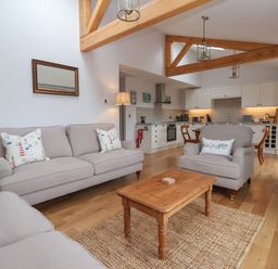 A living room with beige sofas and a wooden coffee table next to a kitchen with white cabinets and wooden beams at Waverley Cottage in Kilnsea near Easington Hull
