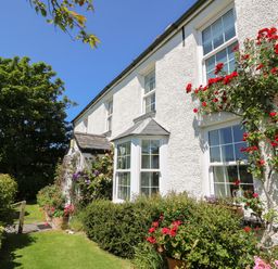 The exterior of a white house with multiple windows surrounded by flowers and bushes at Pen y Graig in Aberporth