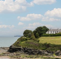 A rocky coastline with grass and trees and a row of white houses at Pen y Graig in Aberporth